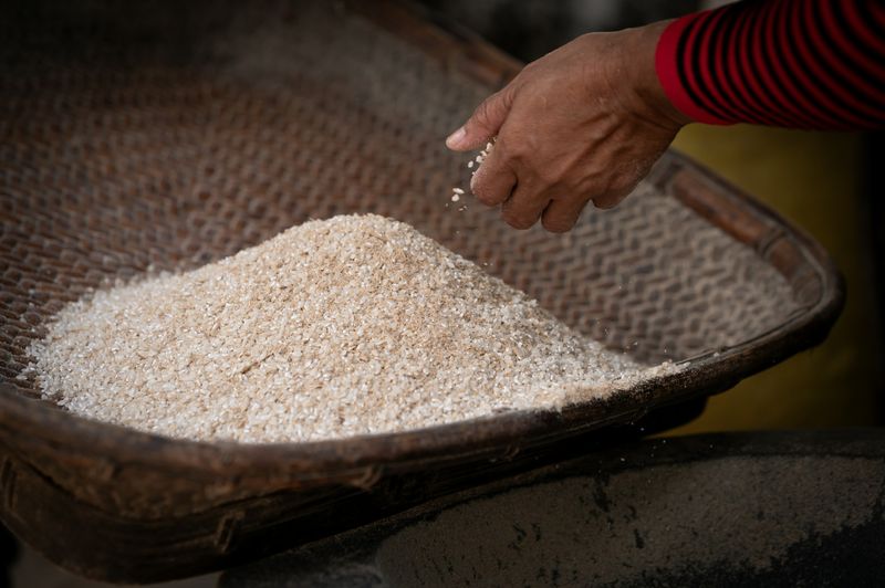 A hand lifting raw rice from a basket